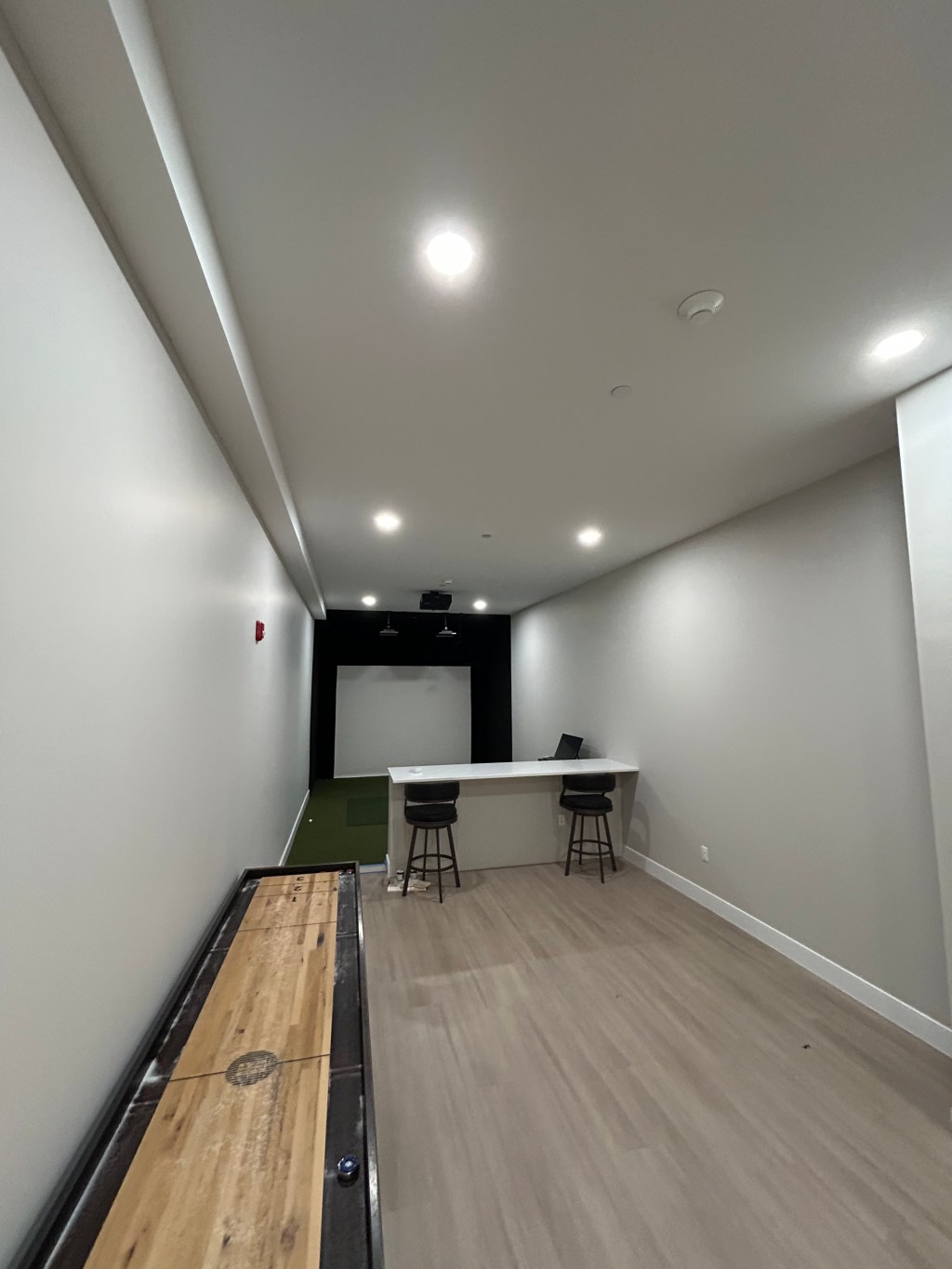 Finished golf simulator and game room with shuffleboard table and bar counter