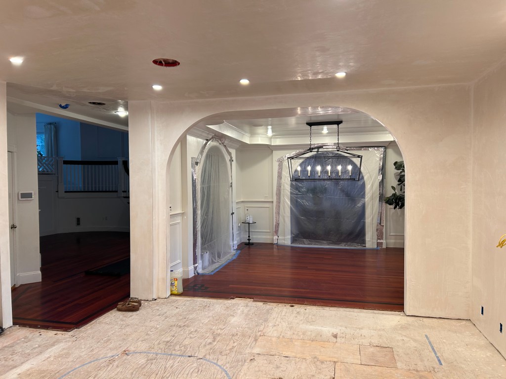 New arched opening with skim-coat plaster walls looking into a dining room